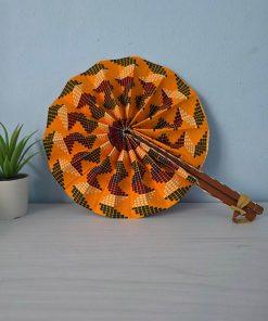 Handcrafted Kente Sunset Fan made from African wax fabric in warm tones, featuring a wooden handle with leather accents.