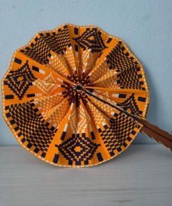 Handcrafted Kente Sunset Fan made from African wax fabric in warm tones, featuring a wooden handle with leather accents.