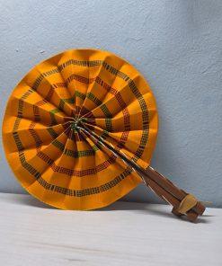 Golden Kente African Fan made from authentic 100% African wax cotton fabric, featuring a pattern inspired by Kente fabric, a wooden handle, and leather details.<br/> <br/> <br/>